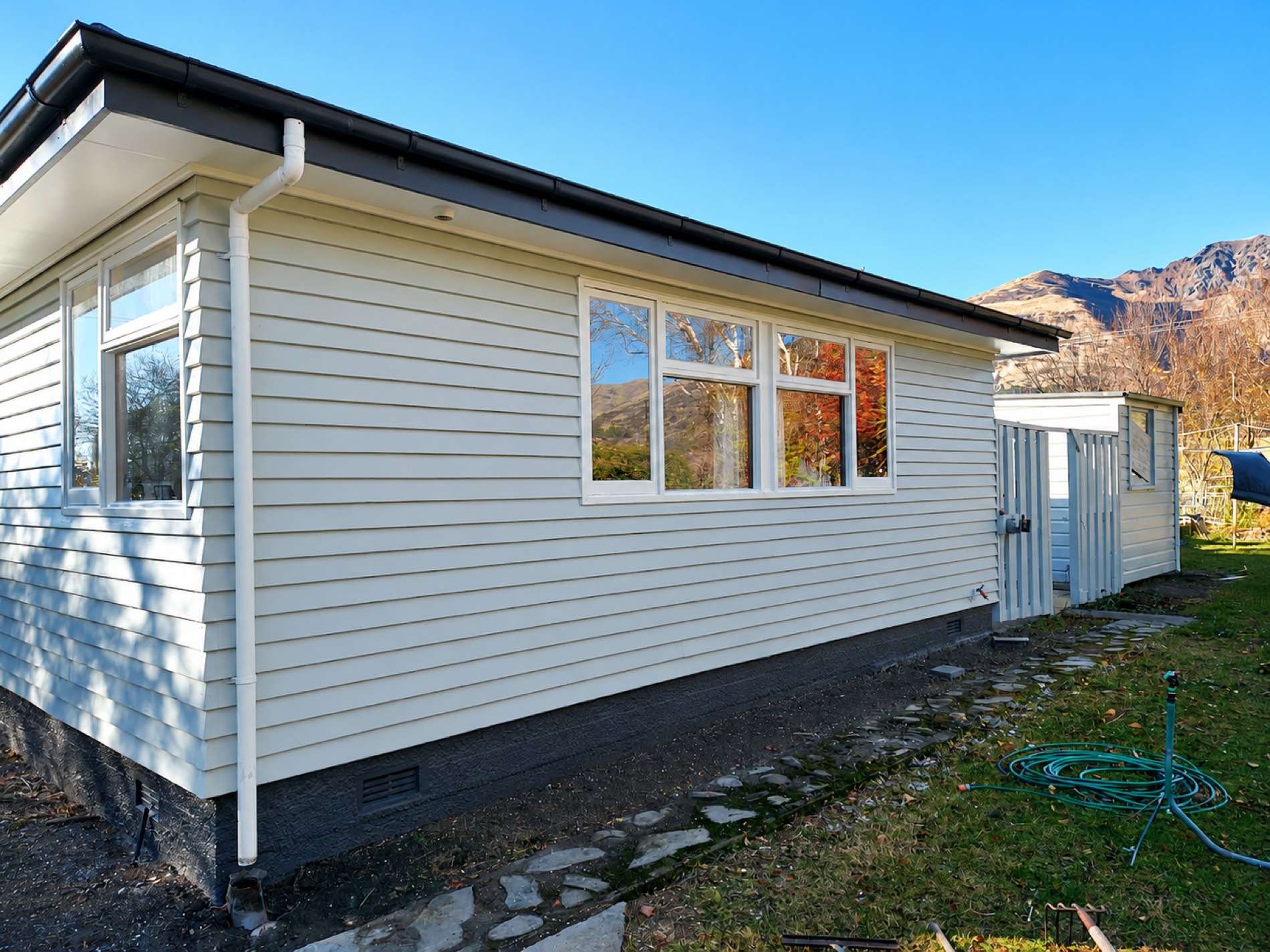 Cream repainted weatherboard home with dark trim and mountain backdrop